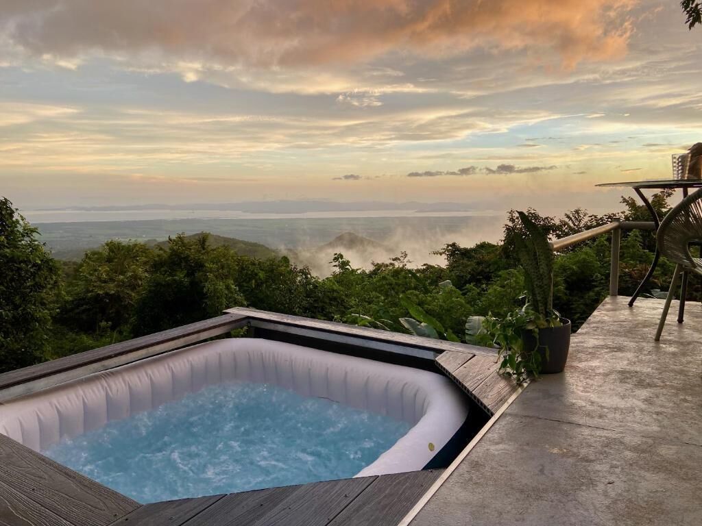 Un jacuzzi en una terraza de madera con vista al océano y a las colinas.