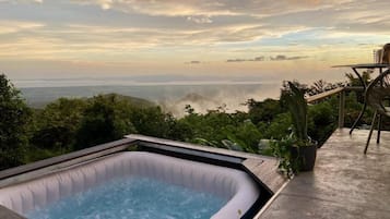 Un jacuzzi en una terraza de madera con vista al océano y a las colinas.