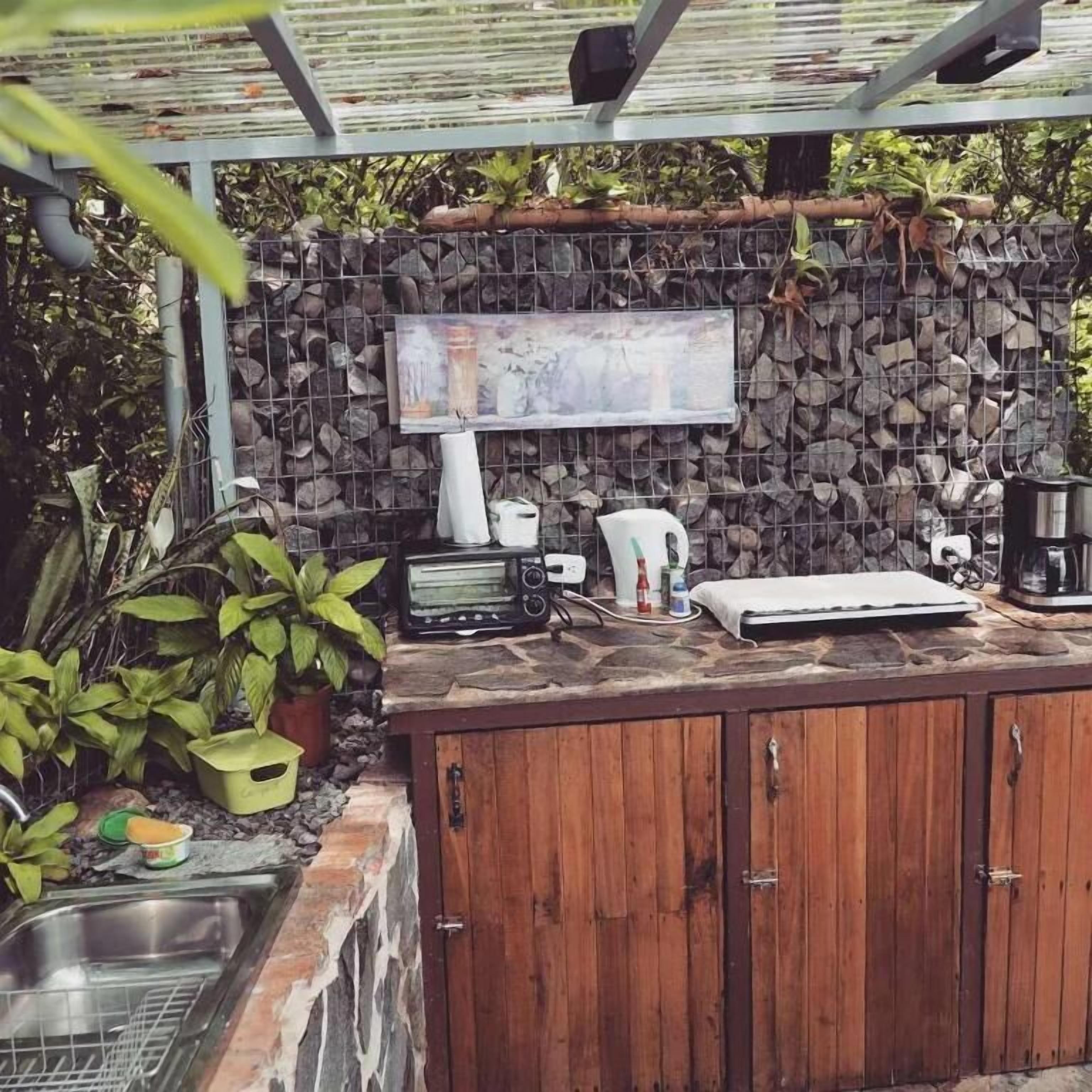 An outdoor kitchen with a stone wall, wooden cabinets, and a built-in grill.