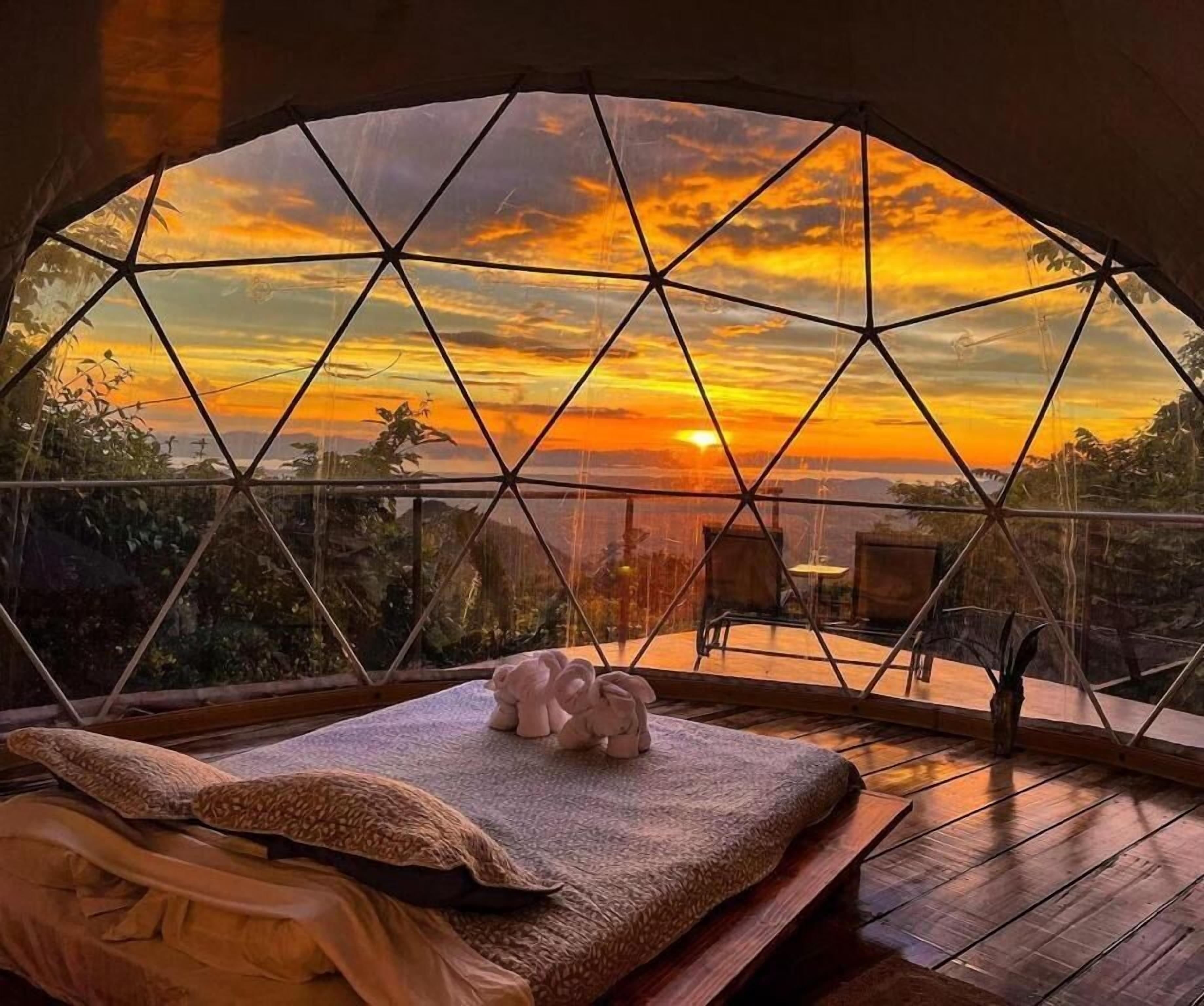 Habitació d'una cúpula geodèsica amb un llit, almoades i vistes a un capvespre.