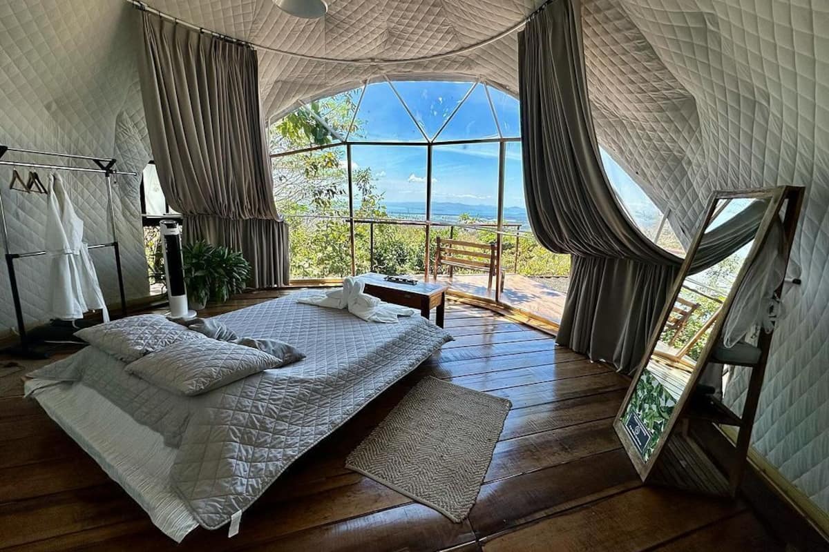 Amplia habitación con tienda, una cama grande, piso de madera y vistas al exterior.