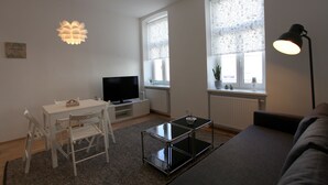 Ein modernes Wohnzimmer mit Flachbildfernseher, Glastisch, einer Couch und einem Essbereich mit Stühlen.