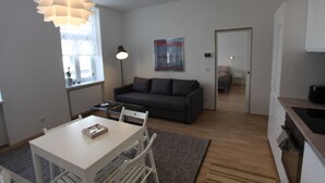 Ein modernes Wohnzimmer mit einer Couch, einem Esstisch mit Stühlen, einer Pendelleuchte, einem Bild an der Wand und einer Küchenzeile mit Herd.