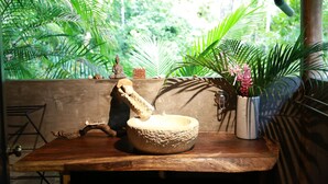 Une table en bois rustique, sur laquelle reposent un mortier et un pilon en pierre, une petite statue de Bouddha et une plante en pot aux fleurs roses.