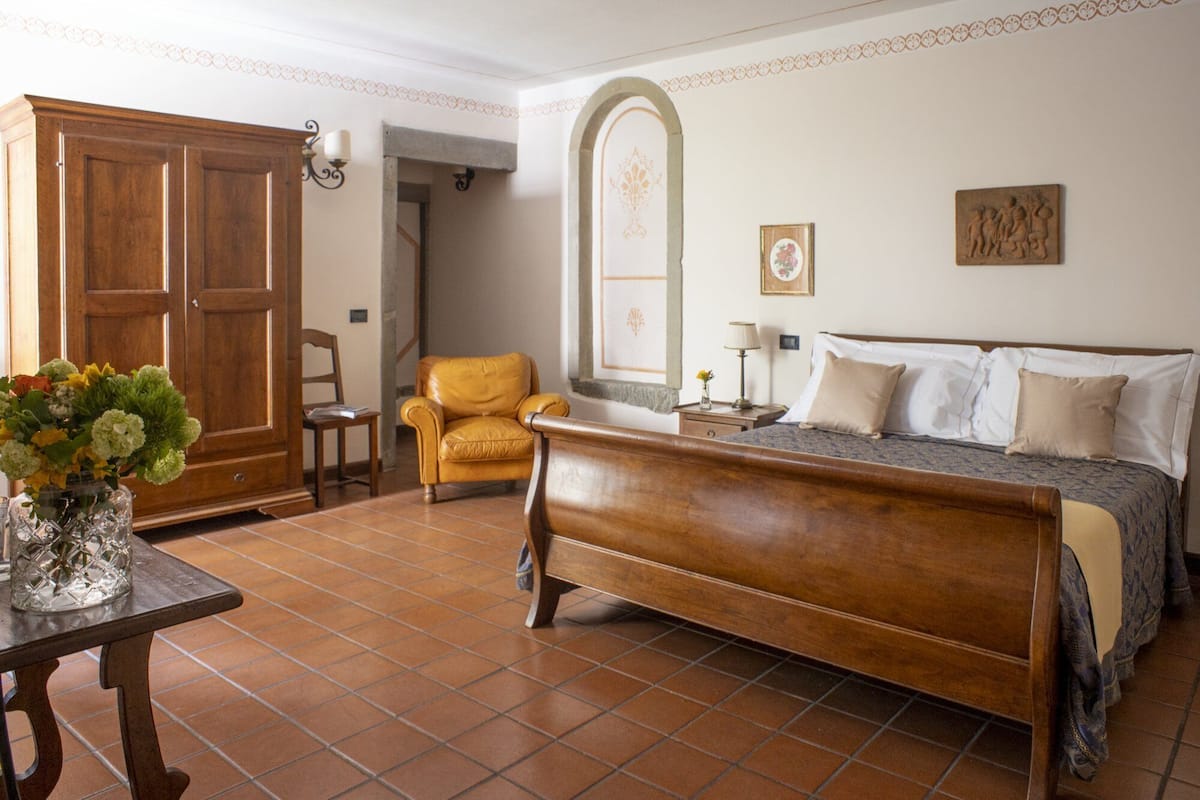 A bedroom with a wooden bed, a chair, a table with a vase of flowers, and a wardrobe.