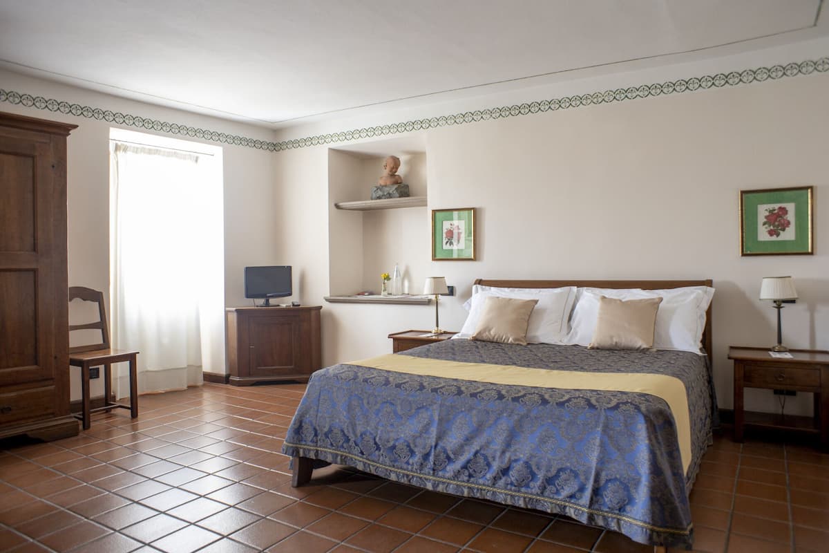 A bedroom with a bed, a television on a cabinet, a dresser, and a window with curtains.