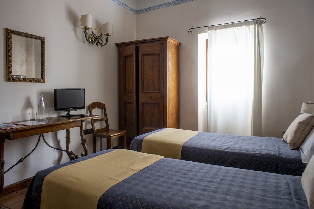 A room with two beds, a desk with a computer, a wardrobe, and a window with curtains.
