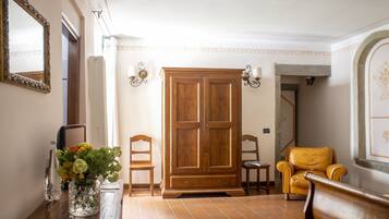 Une pièce comprenant une armoire en bois, deux chaises, une table ornée d’un vase de fleurs et un miroir accroché au mur.