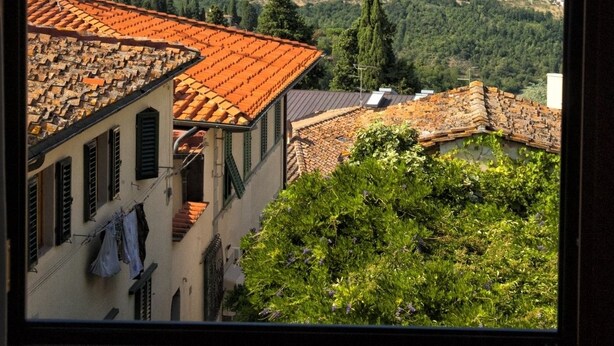 Vista de un pueblo en una ladera con edificios de tejados de terracota, una imponente aguja de iglesia y un cielo azul despejado.