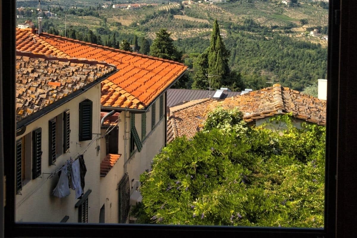 A view of a hillside town with terracotta-roofed buildings, a prominent church steeple, and a clear blue sky.