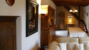 A narrow hallway with a dining table set for two, wooden cabinets, a staircase, and a tapestry on the wall.