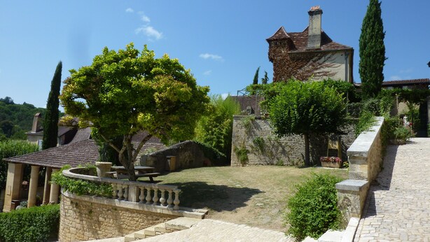 A stone building with a tiled roof, surrounded by greenery and a cobblestone path.