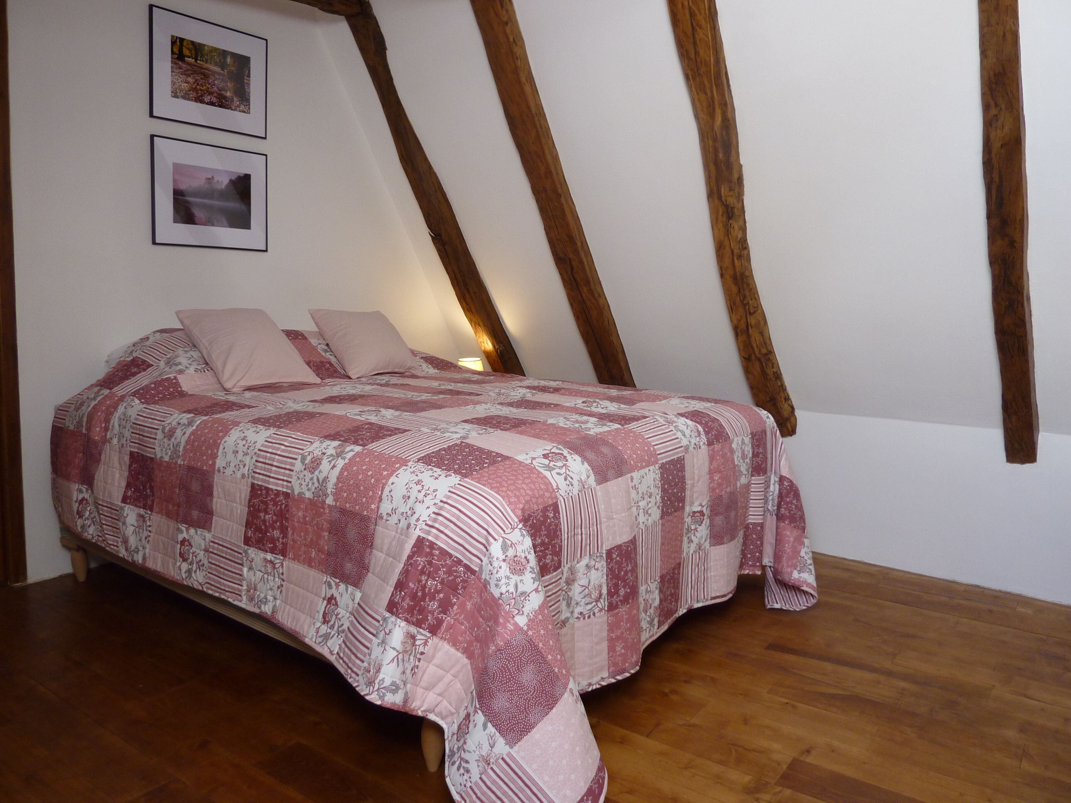 A bedroom with a wooden ceiling, a bed with a pink and white quilt, and two framed pictures on the wall.