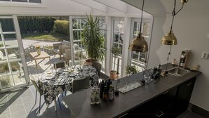 A modern kitchen with a large island, a dining area with a table and chairs, and a view of a garden through large windows. - Business Home Club (Lidköping)