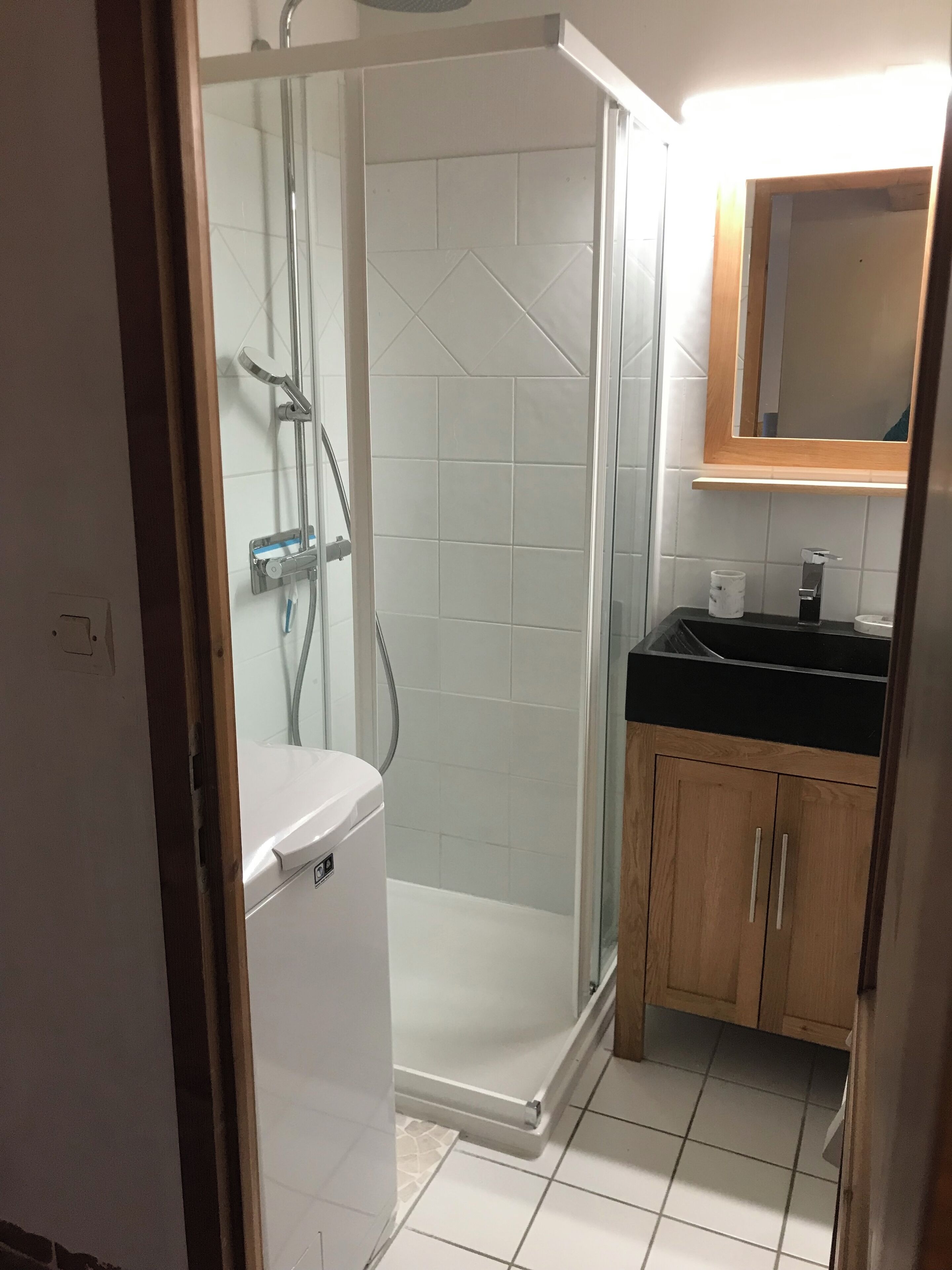 A bathroom with a glass-enclosed shower, a white toilet, a wooden cabinet, and a mirror above the sink.