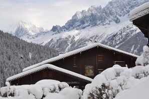Una cabaña de madera con techo inclinado, rodeada de árboles nevados y montañas.