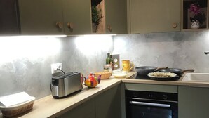 Une cuisine avec des meubles de rangement verts, un grille-pain, une bouilloire, une poêle et un évier.