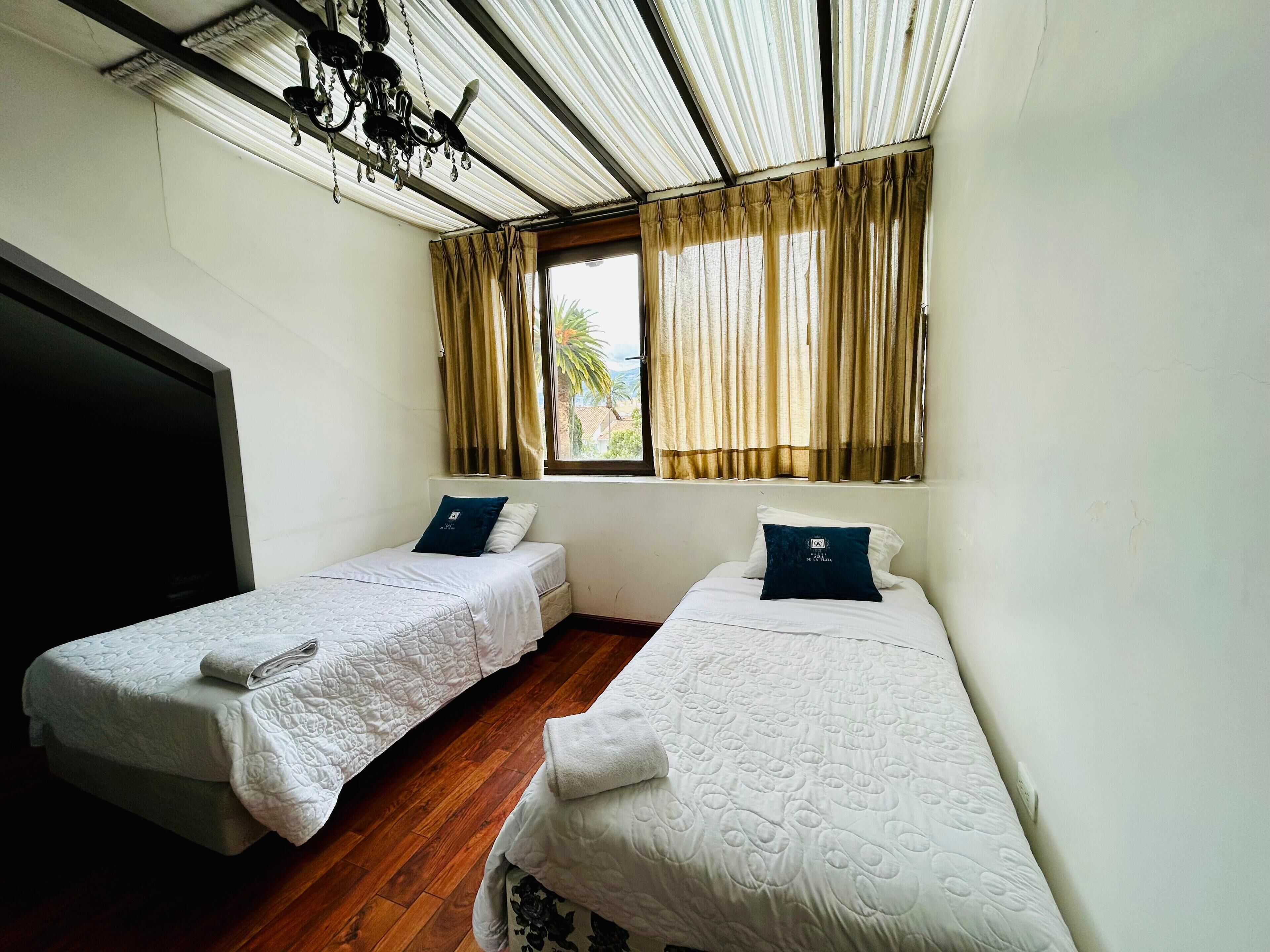 A room with two single beds, a ceiling fan, and a window with curtains.