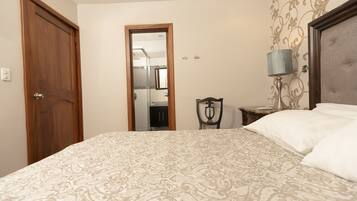 A bedroom with a patterned bedspread, a wooden door, a mirror, a bedside lamp, and a headboard.