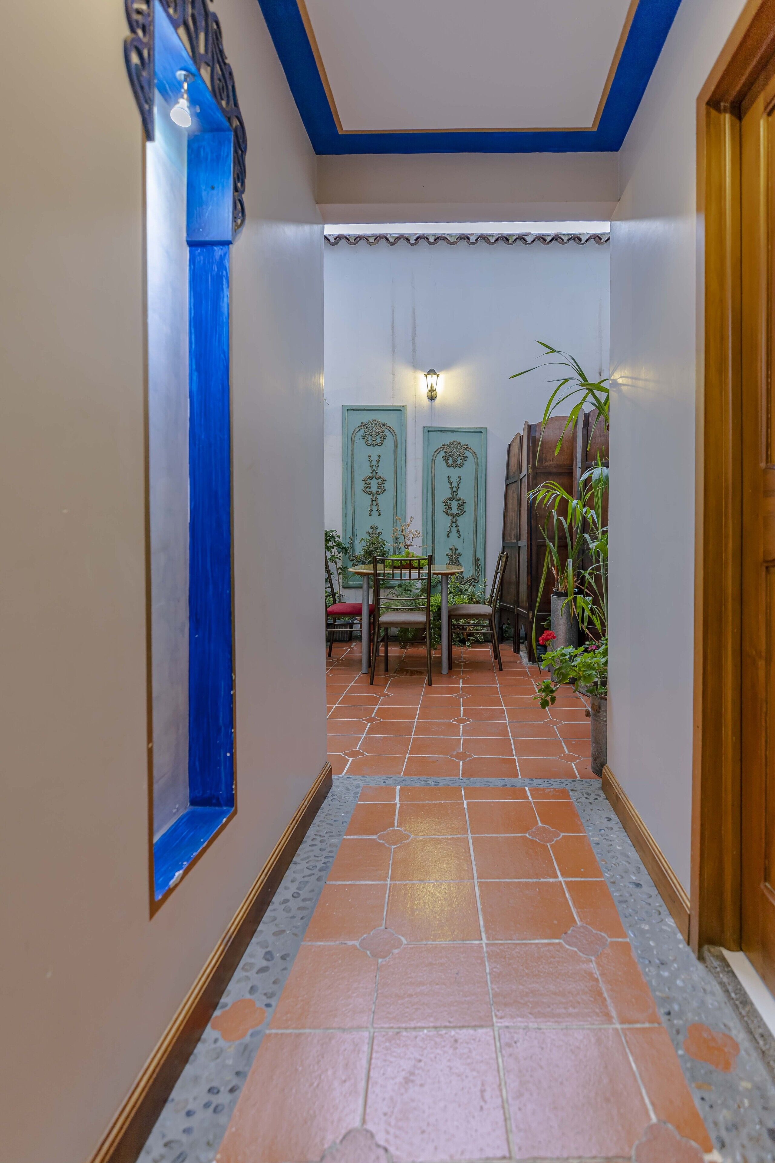 A hallway with tiled flooring, a blue accent wall, and a door leading to a room with a bed.