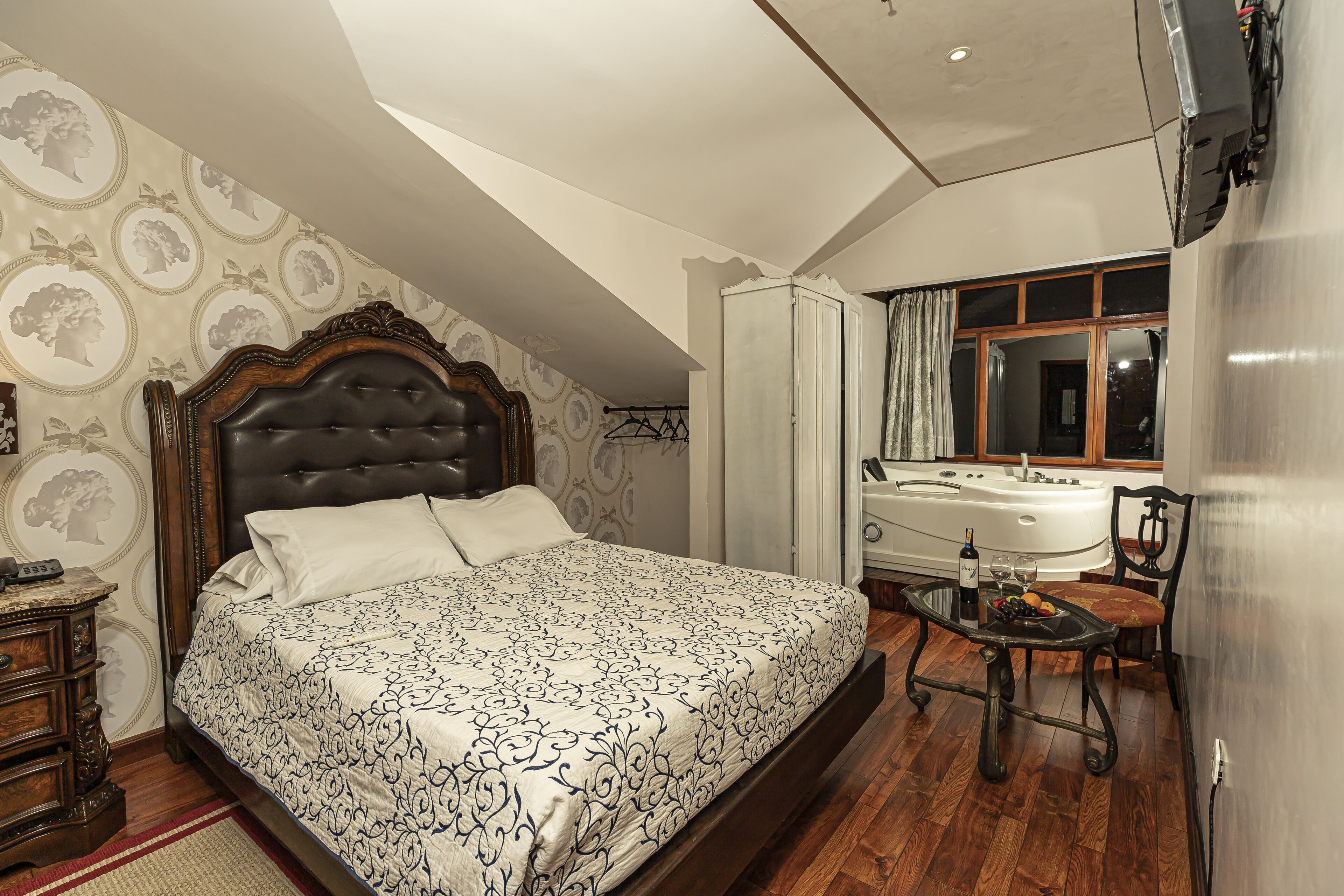 A bedroom with a large bed, a wooden dresser, a vanity with a mirror, a bathtub, and a window with curtains.