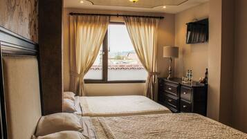 A hotel room with a bed, a dresser, a lamp, and a window with curtains.