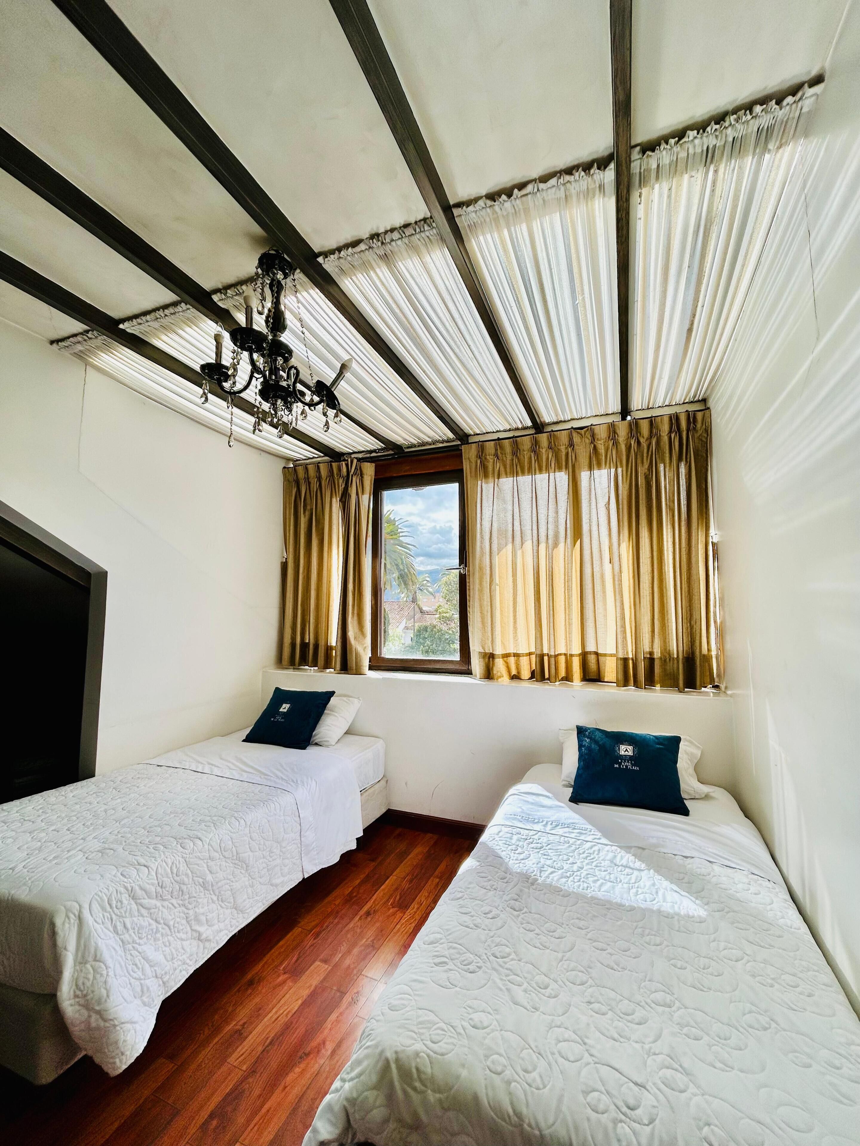 Une chambre avec deux lits simples, un plancher en bois, un ventilateur de plafond et une fenêtre avec des rideaux.
