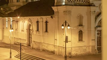 Vista noturna de um edifício histórico com cúpula e torre de sino, com uma escadaria que leva à entrada.