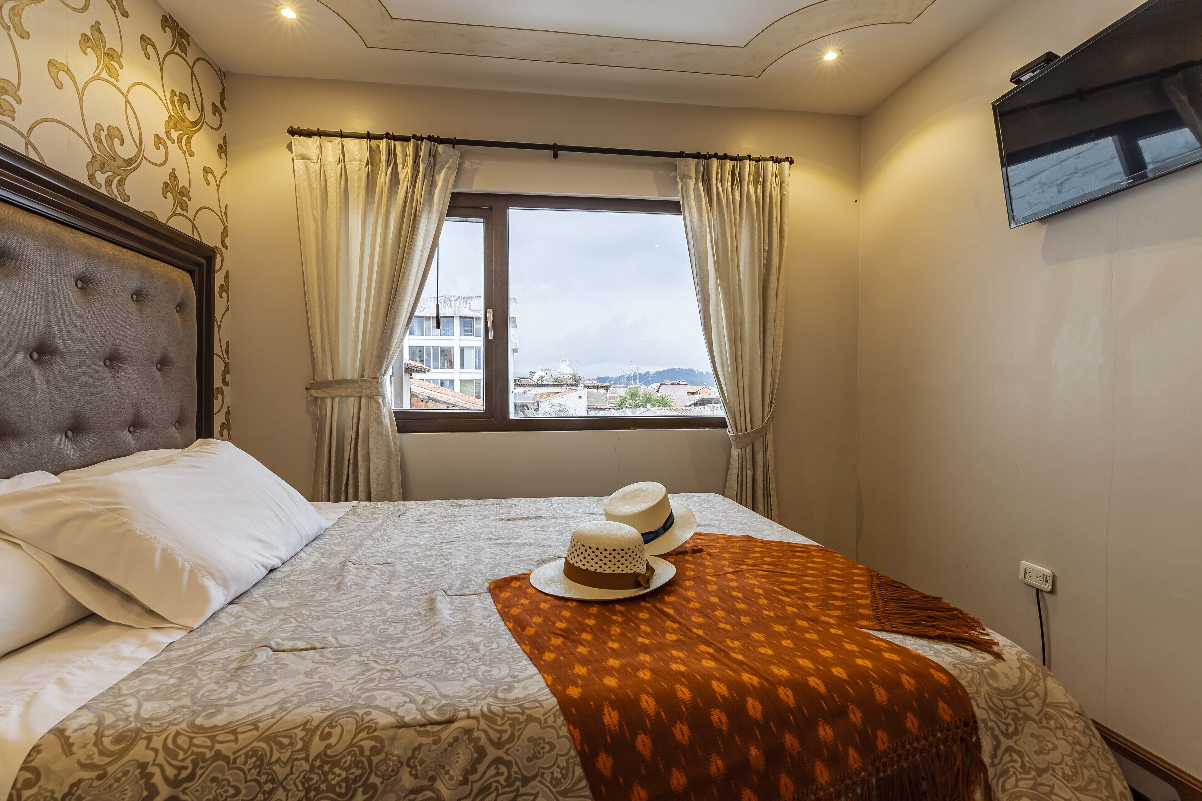 Een hotelkamer met een groot bed, uitzicht op de stad door een raam en een flatscreen televisie aan de muur.