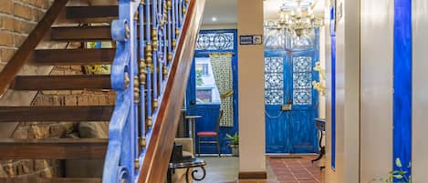 Una escalera de madera con barandillas azules que lleva a una habitación con puerta azul y un candelabro.