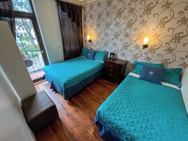 Habitación de hotel con dos camas, suelo de madera, balcón con vistas y papel tapiz estampado.