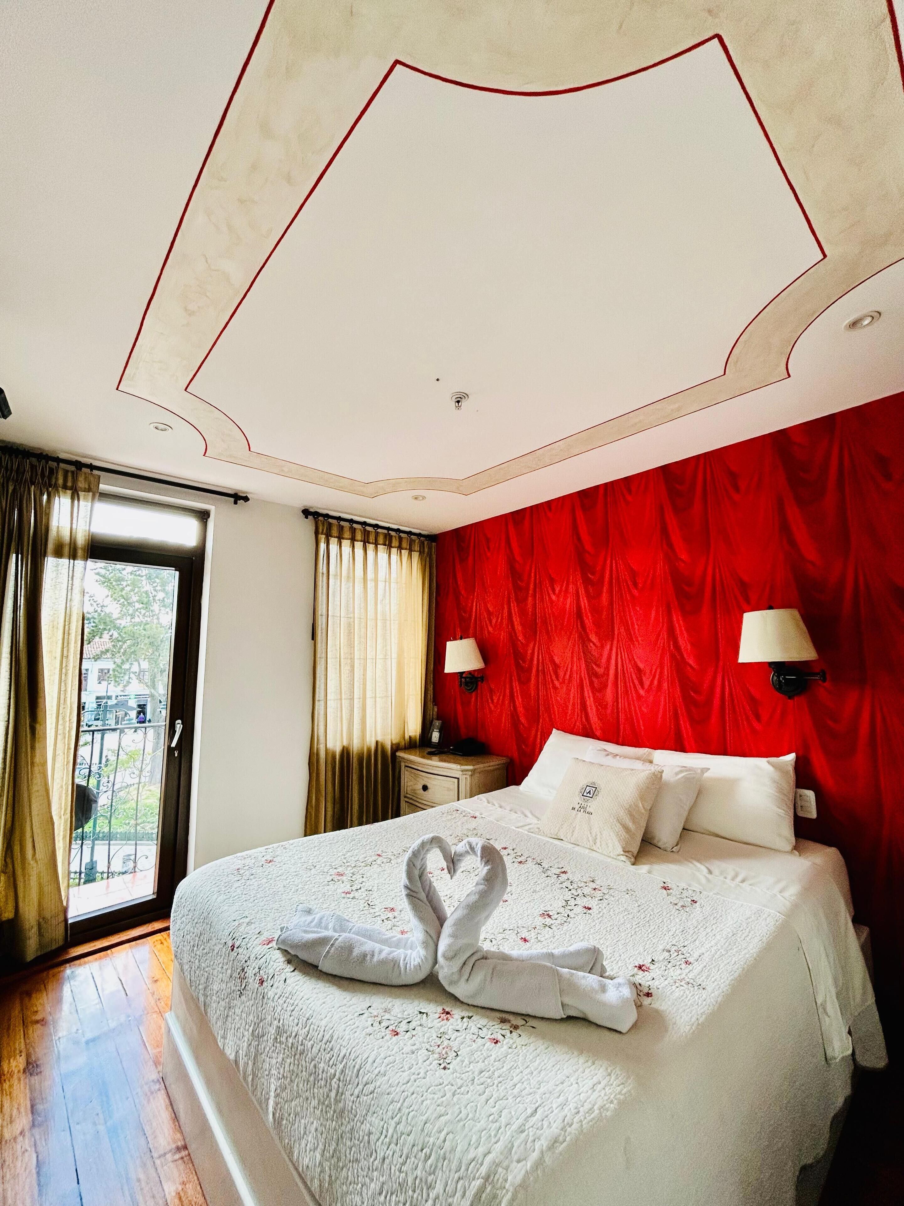 Een hotelkamer met een groot bed, rode gordijnen, een houten vloer en uitzicht door een glazen deur.