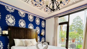 A bedroom with a large bed, a wooden headboard, a chandelier, and a balcony with a view of greenery. - Hotel Azul de la Plaza (Cuenca)
