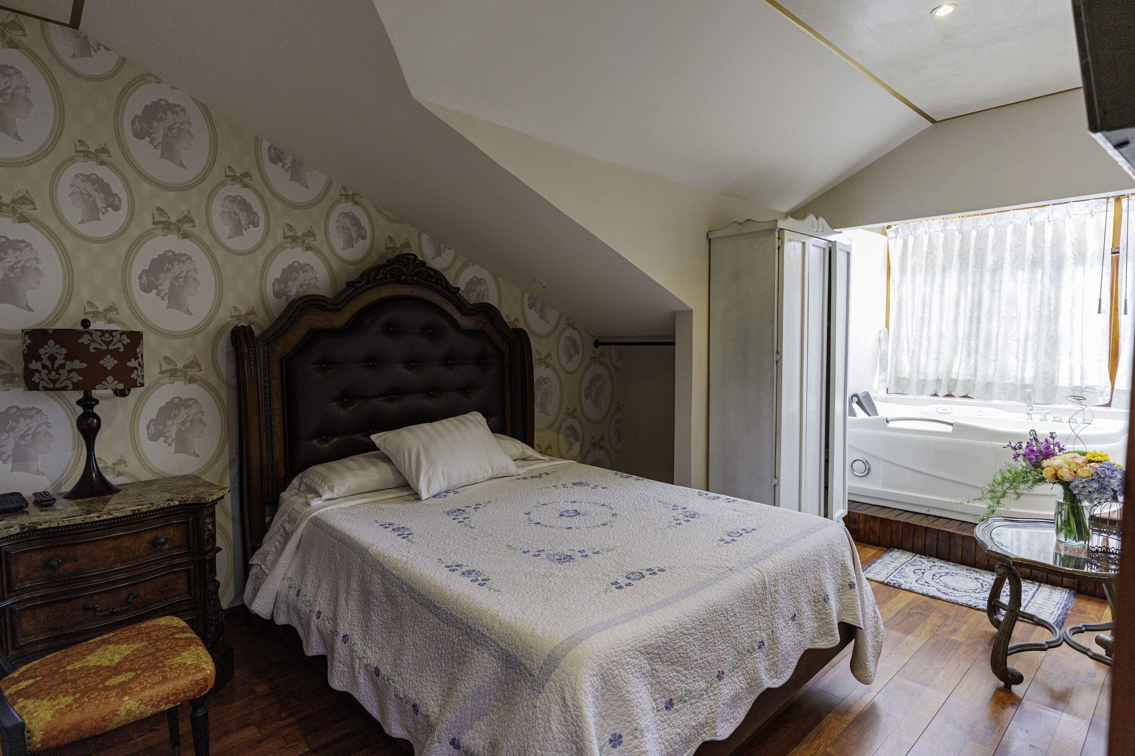 Una camera da letto con un letto grande, un comodino, una cassettiera, una panca e una finestra vista vasca.
