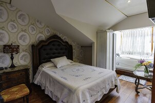 Una camera da letto con un letto grande, un comodino, una cassettiera, una panca e una finestra vista vasca.