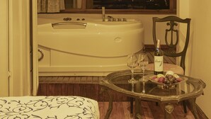 A room with a bathtub, a glass table with a bottle and glasses, and a view of a cityscape at night. - Hotel Azul de la Plaza (Cuenca)