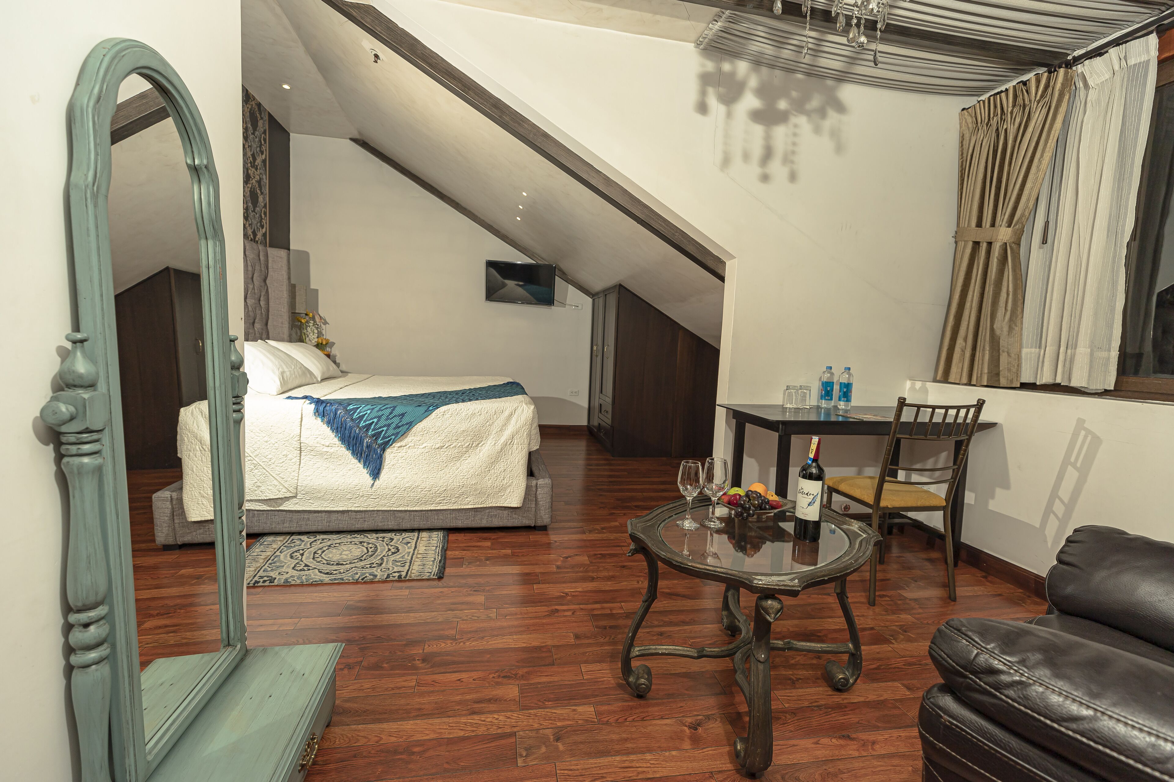 Une chambre à coucher avec un lit, un miroir, une table avec des verres et une bouteille, et un canapé en cuir.