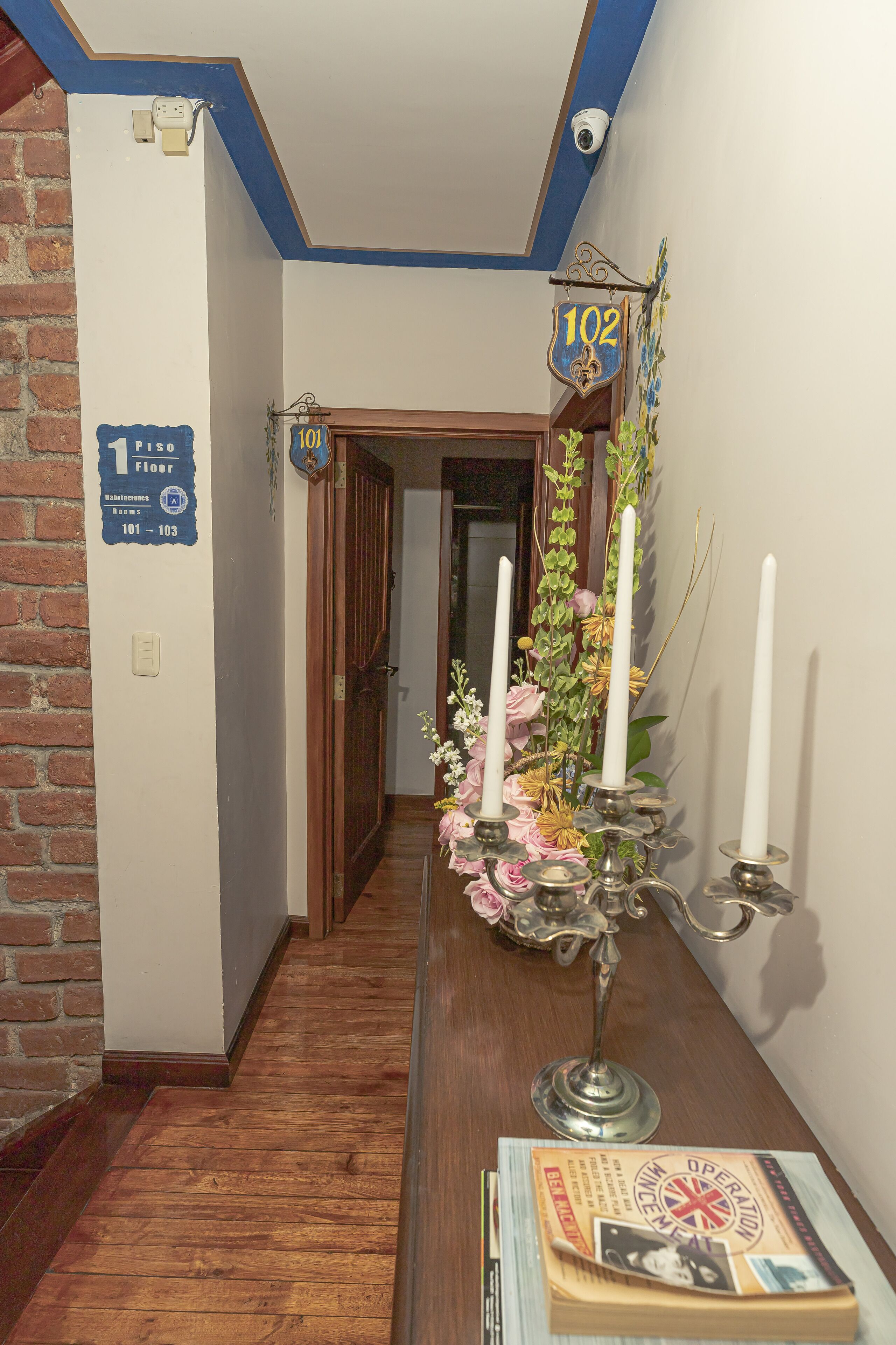 A hallway with a wooden floor, a brick wall, and a sign indicating room numbers 101-103.