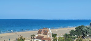 A coastal view with a beach, a stone building with a sloped roof, and a clear blue sky.