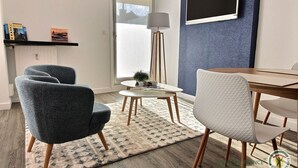 Una sala de estar moderna con una mesa redonda, dos sillones, una lámpara de pie y una estantería con libros.