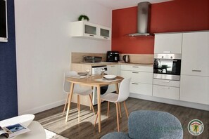 A modern kitchen with white cabinets, a red accent wall, and a dining area with a wooden table and white chairs.