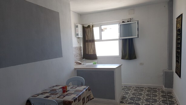 Habitació petita i senzilla amb cuineta, zona de menjador amb taula i cadires, i un paviment amb disseny.