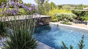 A pool with a stone wall and plants, surrounded by greenery and a clear sky. - Modern villa with private pool between Bonifacio and Porto-vecchio (Figari)