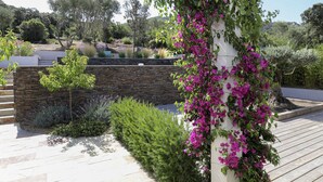 A landscaped garden with a stone wall, a wooden deck, and various shrubs and flowers. - Modern villa with private pool between Bonifacio and Porto-vecchio (Figari)