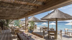 An outdoor dining area with wooden tables and chairs, thatched umbrellas, and a view of the sea. - Modern villa with private pool between Bonifacio and Porto-vecchio (Figari)