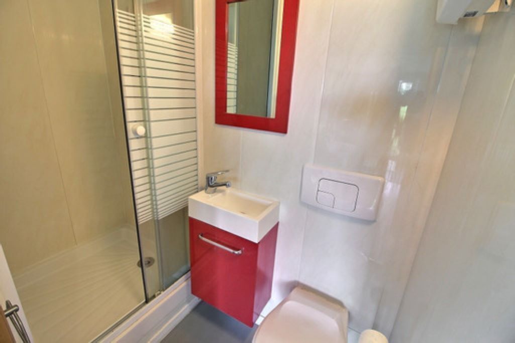 A bathroom with a glass shower enclosure, a white sink with a red cabinet, and a white toilet.