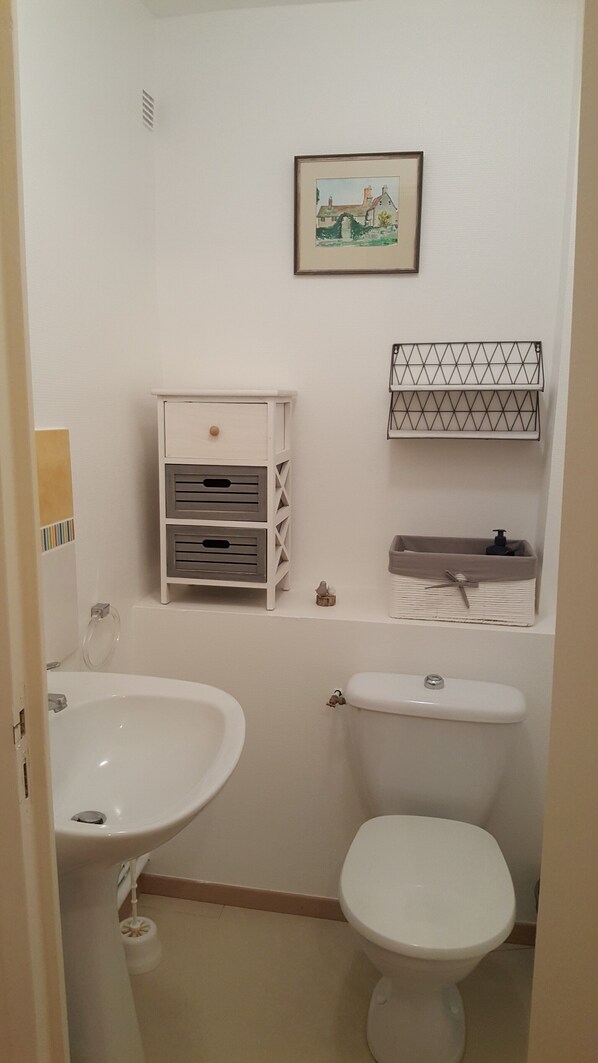 Un bagno con lavandino bianco, wc e un piccolo mobile contenitore con cassetti.