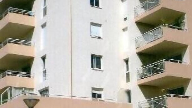 Un edificio de varios pisos con balcones, una entrada con reja y cielo despejado.