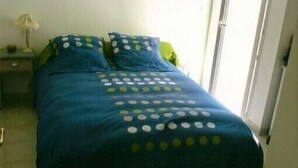 Una cama con colcha azul con lunares blancos, dos almohadas y una mesita de noche con lámpara.
