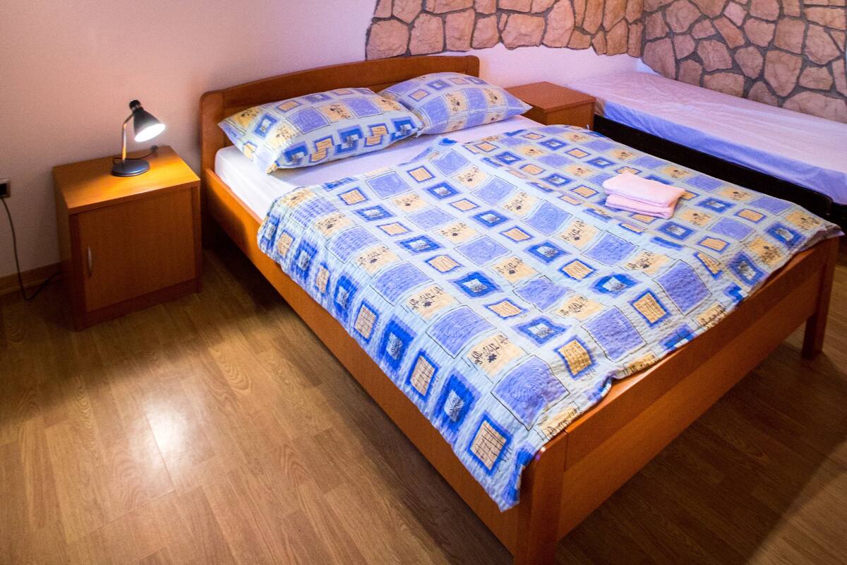 Ein Schlafzimmer mit einem hölzernen Bett, einem Nachttisch, einem steinernen Kopfstück und einer Wand mit einem gerahmten Bild.